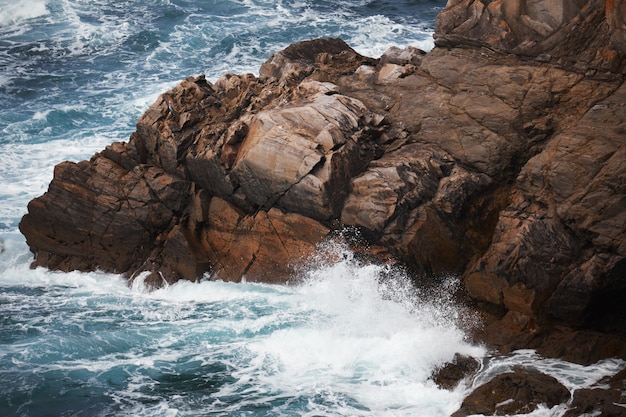 Penhasco rochoso perto de um corpo de água áspero com as ondas espirrando as rochas