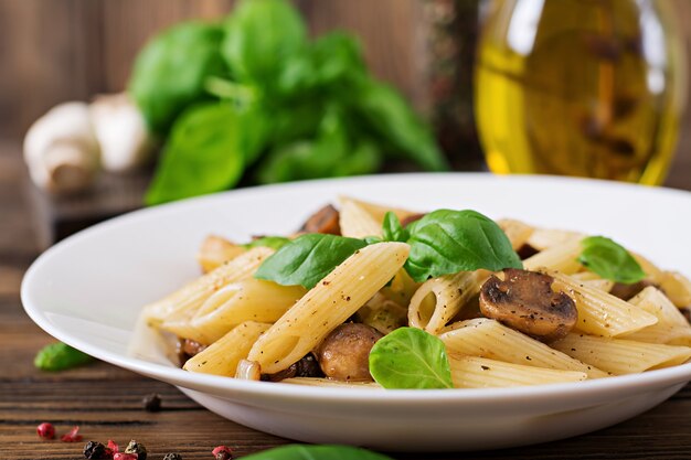 Penne de macarrão vegetal vegetariano com cogumelos em uma tigela branca na mesa de madeira. Comida vegana.