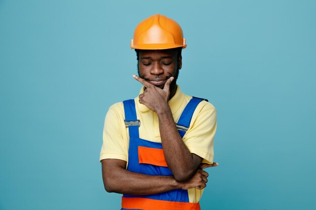 pensando agarrou o queixo jovem construtor americano africano de uniforme isolado em fundo azul