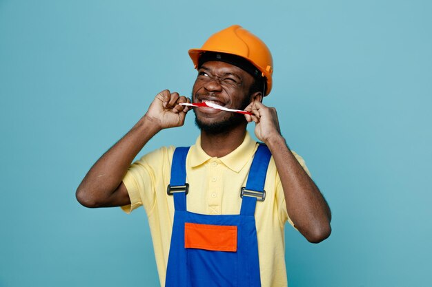 Pensando em colocar fita adesiva na boca jovem construtor americano africano de uniforme isolado em fundo azul