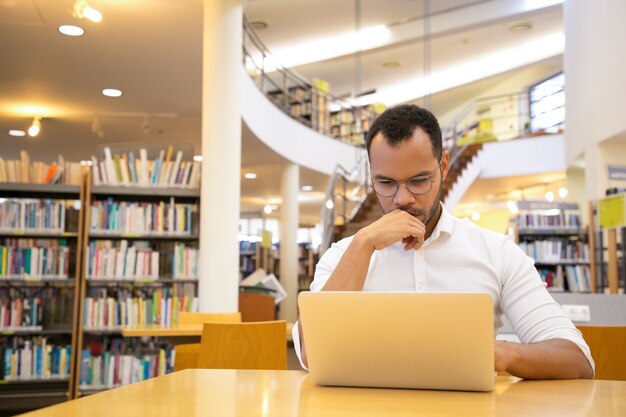 Pensando jovem segurando a mão no queixo e olhando para laptop