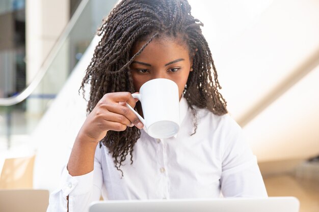 Pensativa jovem trabalhadora bebendo café