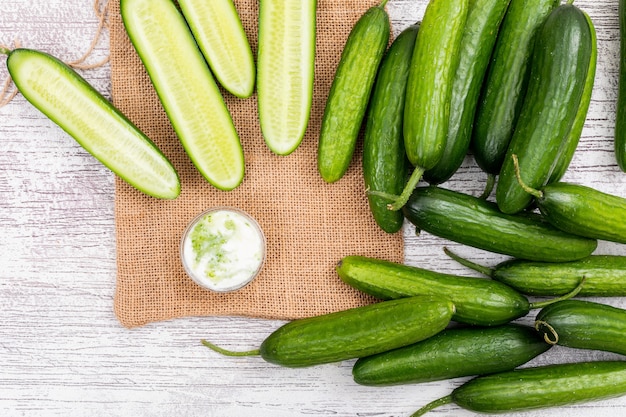 Pepino de vista superior fatiado com iogurte branco em saco de linho bege na horizontal de madeira branca