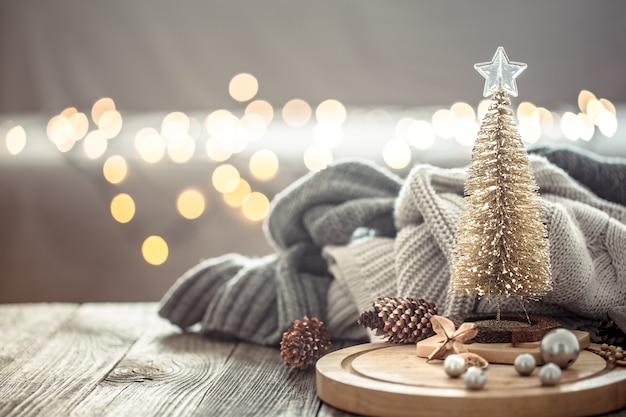 Pequena árvore de Natal sobre bokeh de luzes de Natal em casa na mesa de madeira com camisola na parede e decorações.