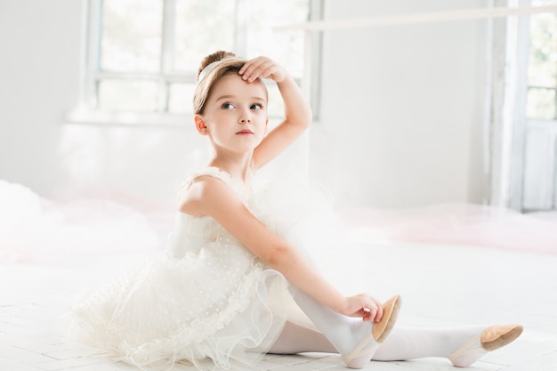 Pequena bailarina com tutu branco na aula na escola de balé