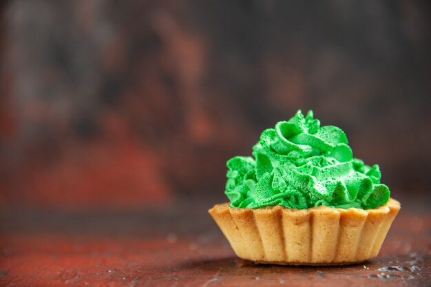 Pequena torta de frente com creme de confeiteiro verde em uma mesa vermelha escura com local de cópia