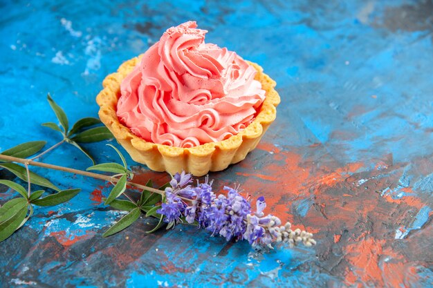 Pequena torta de vista inferior com pastelaria rosa flores roxas na mesa azul, lugar grátis