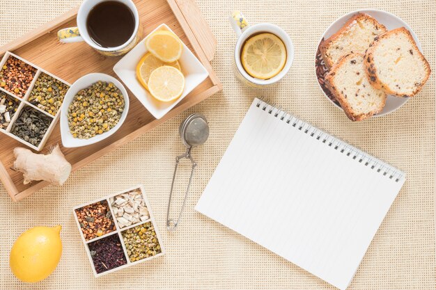 Pequeno-almoço saudável com variedade de ervas; limão; filtro; pão; bloco de notas em espiral de gengibre e em branco