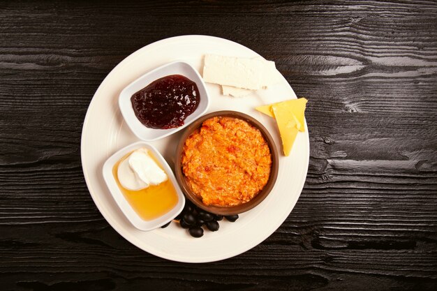 Pequeno-almoço turco menemen com variações de mel, creme, azeitonas, geléia e queijo em chapa branca e copo de chá