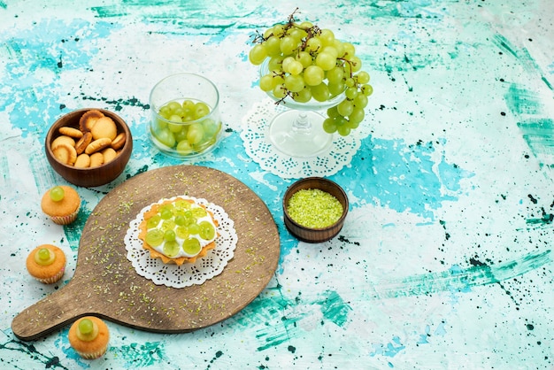 Pequeno bolo com creme delicioso e biscoitos de uvas verdes frescas e fatiados isolados em azul, bolo doce fruta açúcar asse