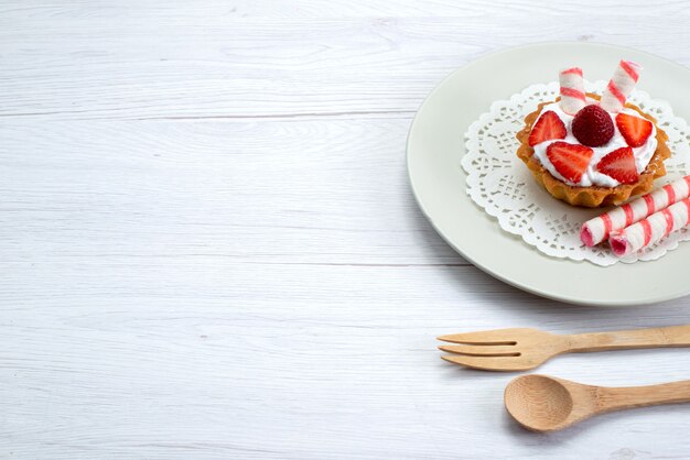 pequeno bolo com creme e morangos fatiados dentro do prato na mesa branca, bolo de frutas doce de baga