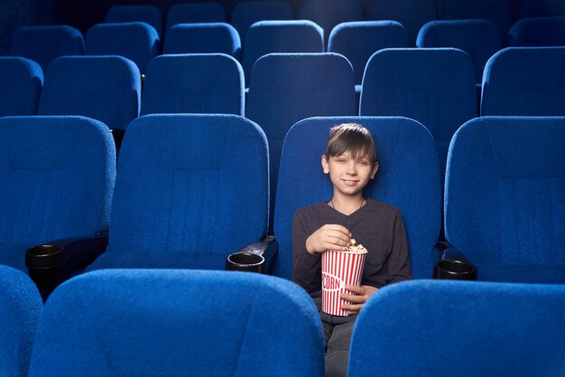 Pequeno espectador masculino sentado sozinho no cinema e sorrindo