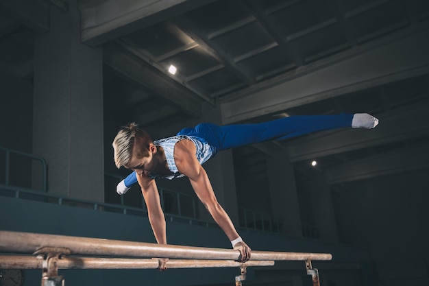 Pequeno ginasta masculino treinando no ginásio flexível e ativo caucasiano apto garotinho atleta em roupas esportivas praticando em exercícios para equilíbrio de força