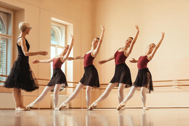 Pequeno grupo de bailarinas praticando com seu professor maduro no estúdio de balé