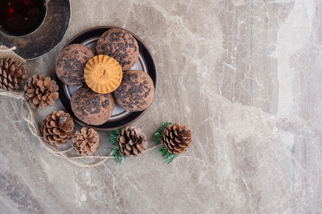 Foto grátis pequeno prato de biscoitos, xícara de chá, molho de pinhas e uma coroa de flores em mármore.