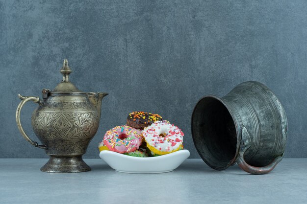 Pequeno prato de donuts entre um bule e uma jarra em mármore.