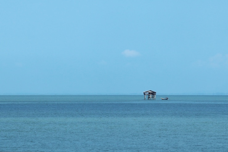 Foto grátis pequeno prédio no mar sob a luz do sol e um céu azul durante o dia