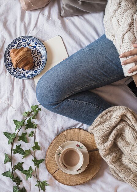 Perna de mulher na cama perto de café e croissant
