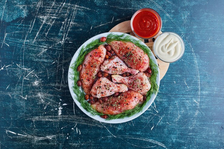 Foto grátis pernas de frango cru com especiarias com ketchup e maionese.