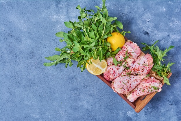 Foto grátis pernas de frango cru com especiarias em uma placa de madeira em azul