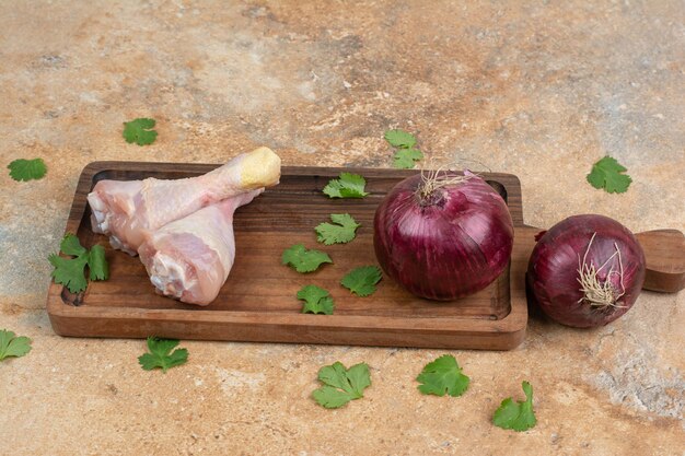 Pernas de frango cru com verduras e cebolas na tábua de madeira