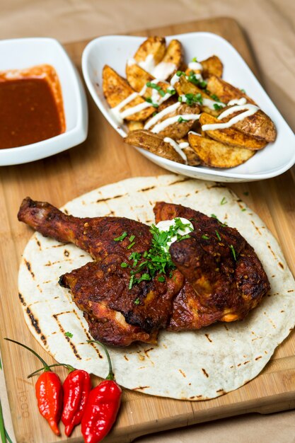 Pernas de frango frito servidas em pão sírio, um prato de batatas e molho de tomate