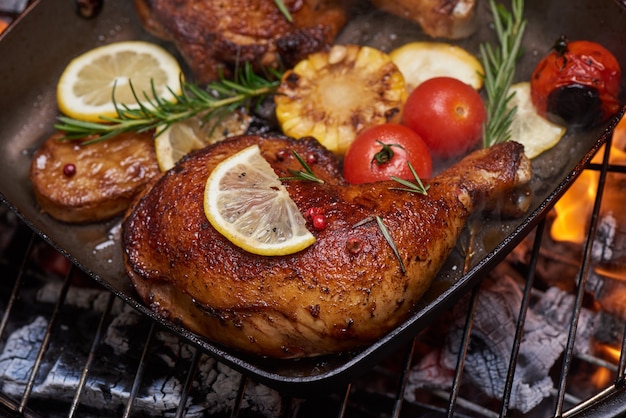 Pernas de frango grelhado na grelha em chamas com legumes grelhados com tomate, batata, sementes de pimenta, sal.