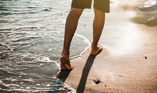 Pernas de homem andando na praia perto da água