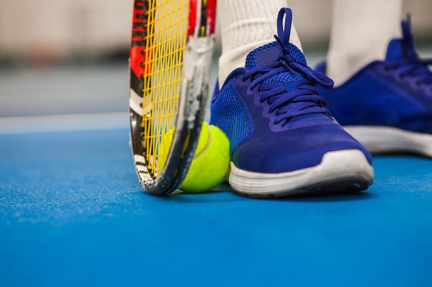 Pernas de jovem em uma quadra de tênis fechada com bola e raquete