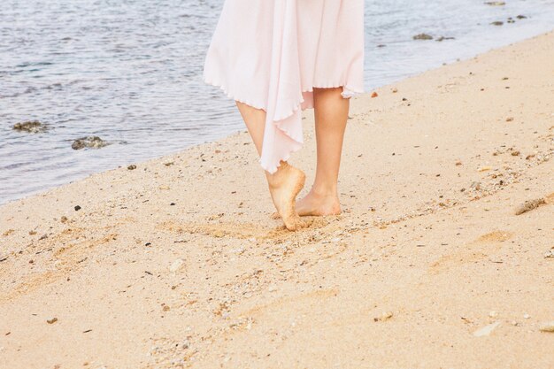 Pernas de mulher caminhando na areia da praia