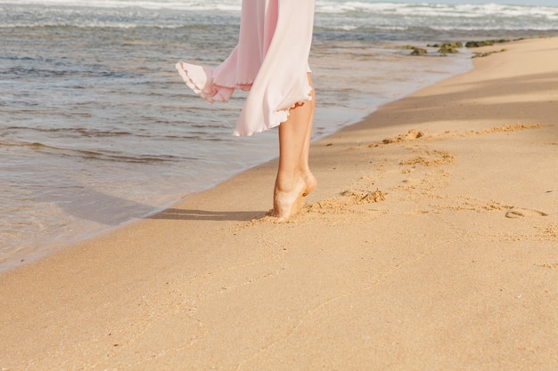 Pernas de mulher caminhando na areia da praia