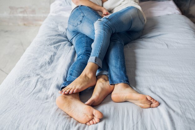 Pernas de um jovem casal deitado na cama em casa em roupas casuais, dormindo de jeans, homem e mulher passando momentos felizes juntos, relaxando, se abraçando, amando e namorando