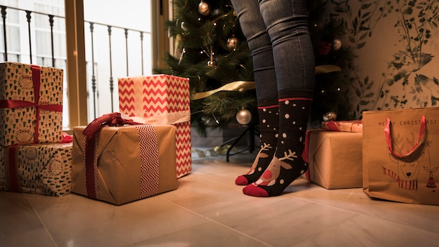 Pernas em meias de Natal entre caixas de presentes e decoradas abeto