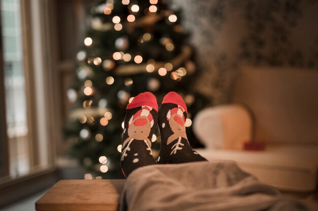 Pernas humanas em meias engraçadas perto da árvore de Natal
