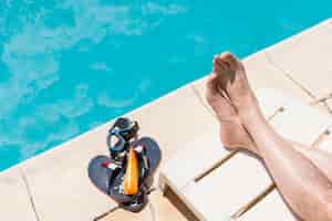 Foto grátis pernas perto de óculos com loção e flip-flops perto da piscina