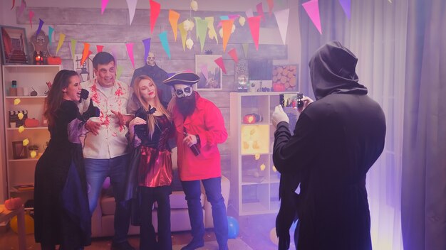Personagens assustadores tirando uma foto de grupo na festa de halloween em um quarto decorado.
