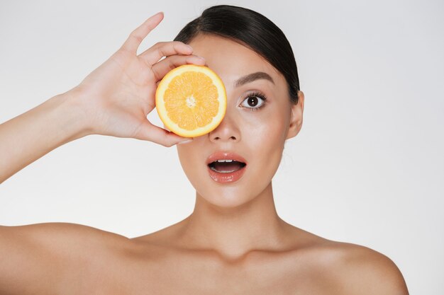 Perto da bela dama com pele fresca macia segurando laranja suculenta, desfrutando de vitamina natural isolada sobre o branco