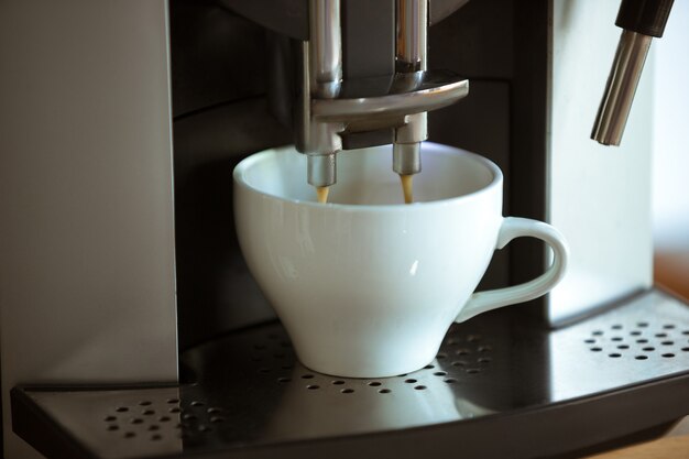 Perto da máquina de café, servindo cappuccino, expresso, americano em xícara branca em casa ou no café. Bebida quente saborosa e aromática. Alimentos, nutrição, bebida mais popular para café da manhã e pausa no trabalho.