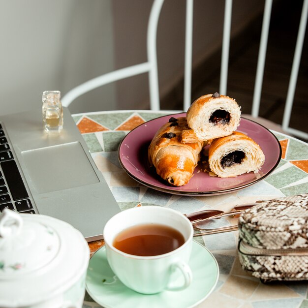 Perto da mesa redonda com croissant de chocolate xícara de chá_ notebook e bolsa