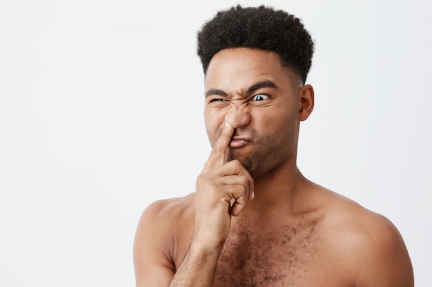 Perto de bobo bonito americano de pele escura com penteado afro e corpo nu, segurando o dedo no nariz, olhando de lado com a expressão estúpida do rosto, sendo por sua vez na manhã.