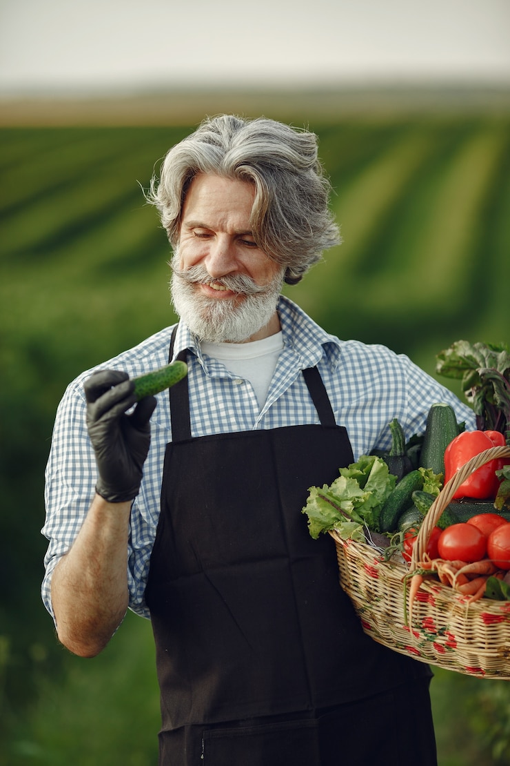 Foto grátis perto do velho fazendeiro segurando uma cesta de legumes. o homem está parado no jardim. sênior em um avental preto.