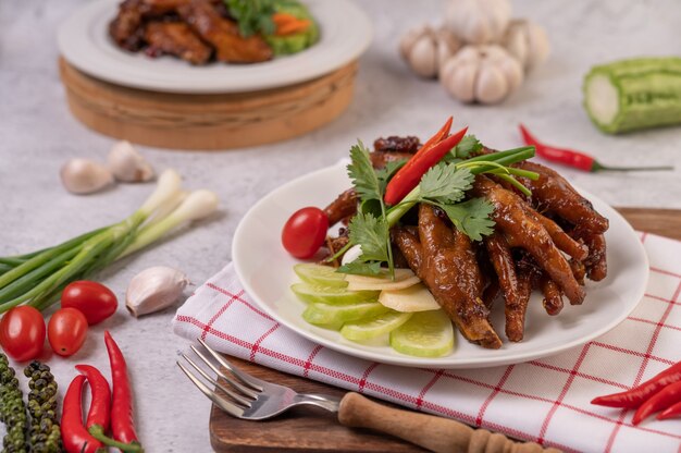 Pés de frango frito doce em um prato branco com coentro, pimenta, pepino e tomate.