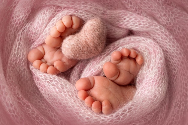 Pés de gêmeos recém-nascidos. dois pares de pés de bebê em um cobertor de malha rosa. coração de malha rosa. close up - dedos, calcanhares e pés de um recém-nascido. irmãos recém-nascidos, irmãs. fotografia macro de estúdio.