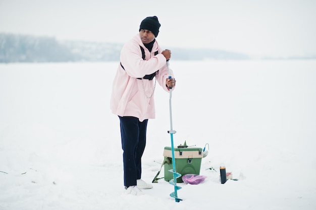 Pescador americano africano fazendo buraco no gelo congelado por broca Pesca de inverno