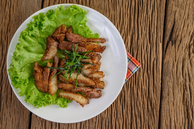Pescoço de porco grelhado em um prato branco sobre uma mesa de madeira.
