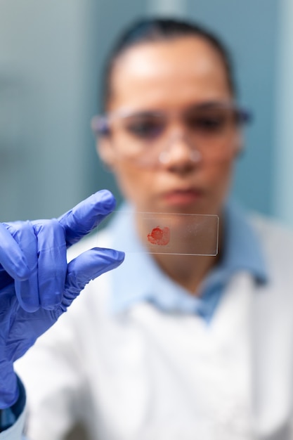 Foto grátis pesquisador químico segurando um copo com amostra de sangue trabalhando em um experimento de microbiologia