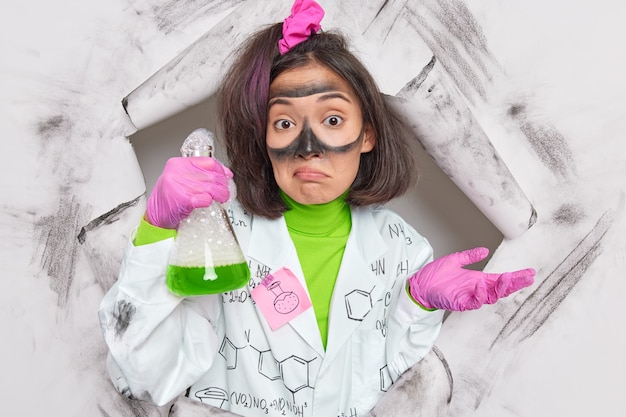 Foto grátis pesquisadora estuda reações químicas sem saber por que obteve tamanha explosão de reagentes desenvolve novos produtos em poses de laboratório através de buraco de papel vestida de uniforme