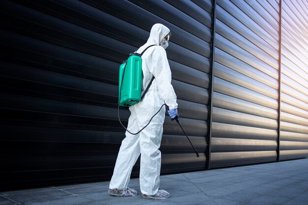 Pessoa com roupa de proteção química branca fazendo desinfecção e controle de pragas com pulverizador para matar insetos e roedores