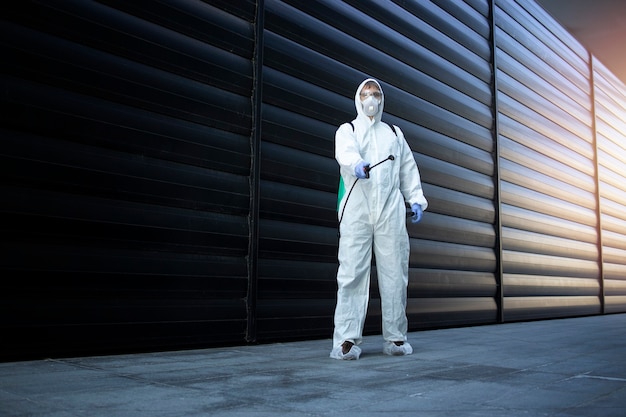 Pessoa com roupa de proteção química branca fazendo desinfecção e controle de pragas e pulverizando veneno para matar insetos e roedores