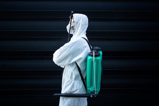 Pessoa com roupa de proteção química branca segurando um pulverizador com produtos químicos desinfetantes para impedir a propagação de vírus altamente contagiosos